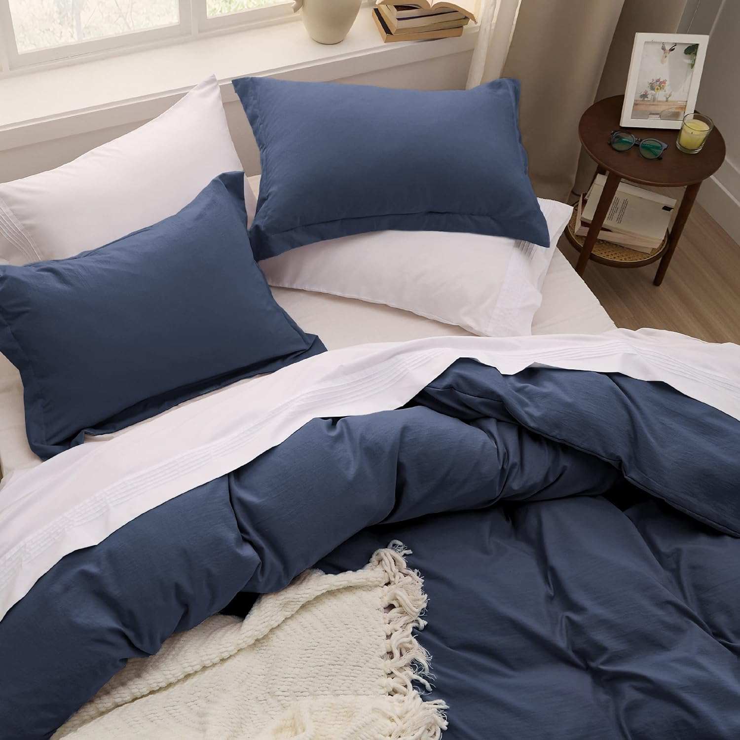 Cozy bedroom with navy blue and white bedding, featuring soft pillows and a fringed throw blanket, creating an inviting and comfortable space.