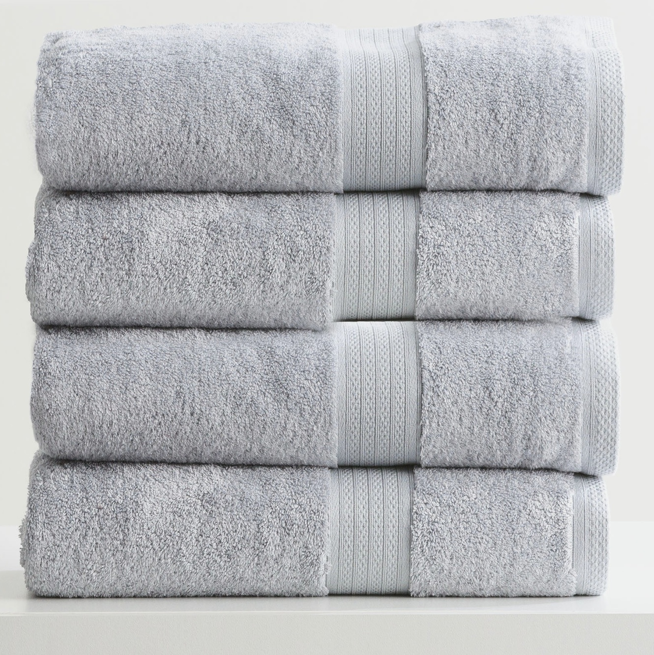 Stack of four soft, grey towels neatly folded on a white surface