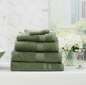 Stack of green bath towels in a modern bathroom with white flowers in a vase