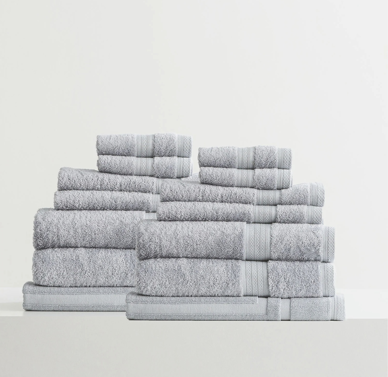 Set of neatly stacked gray bath towels in various sizes on a white surface.